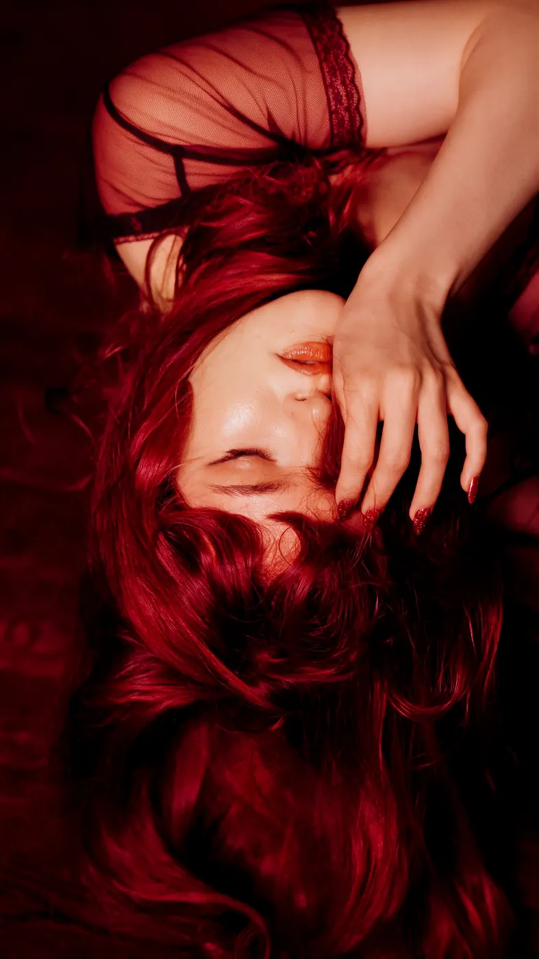 A performer with red hair lying back, a hand across her eyes, in red light
